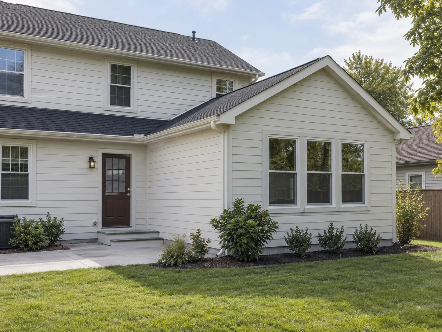 Two-story house with a single-story addition on the side, matching siding and a row of three windows